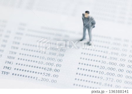 Miniature businessman standing on financial statement numbers, reviewing accounts and audit results. Concept of accounting, tax, risk management and budget control with copy space, soft focus. 136388141