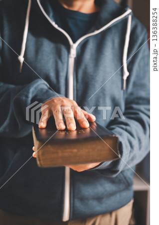 Man holding an open Bible and turning pages, warm indoor light and shallow depth of field, symbolizing Christian faith, devotion, scripture study and quiet worship at home. Man holding an open Bible and turning pages, warm indoor light and shallow depth of field, symbolizing Christian faith, devotion, scripture study and quiet worship at home. 136388254