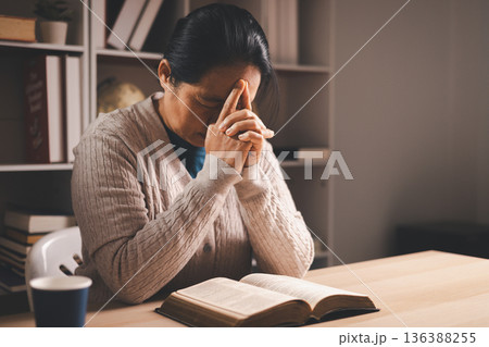 Stressed woman with hand on face beside an open Bible and glasses on a desk, warm indoor light and copy space, expressing grief, prayer, faith and seeking comfort during quiet reflection at home. Stressed woman with hand on face beside an open Bible and glasses on a desk, warm indoor light and copy space, expressing grief, prayer, faith and seeking comfort during quiet reflection at home. 136388255