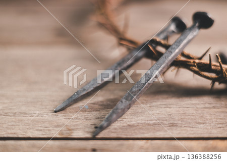 Crown of thorns with iron nails and a hammer on rustic wooden table, dramatic light and copy space, symbolizing crucifixion, sacrifice, Easter, Good Friday, Holy Week and Christian faith. 136388256