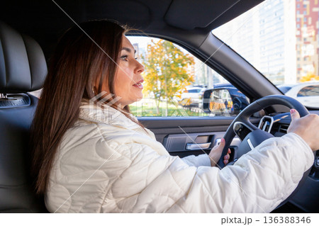 woman with long brown hair driver in a modern car. woman looks ahead at the road. Safe driving behavior and road trip. delivery, women's taxi woman with long brown hair driver in a modern car. woman looks ahead at the road. Safe driving behavior and road trip. delivery, women's taxi 136388346