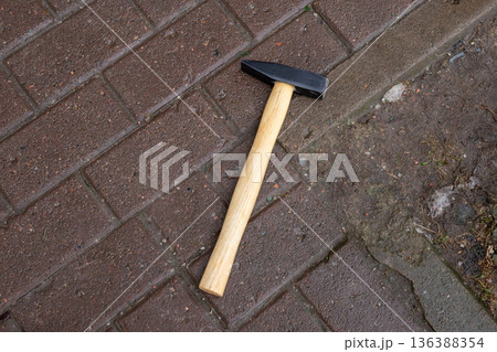 Hammer with wooden handle lying on wet brown paving stones. Hand tool for construction and repair work concept. Top view 136388354