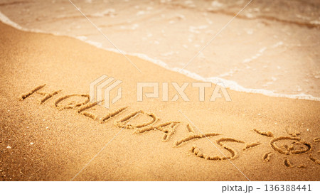 The word holidays written in the sand on a beach The word holidays written in the sand on a beach 136388441