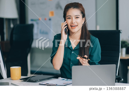 Determined asian businesswoman works late in a modern office, confidently analyzing data on her laptop, embodying success and professionalism with a smile Determined asian businesswoman works late in a modern office, confidently analyzing data on her laptop, embodying success and professionalism with a smile 136388887