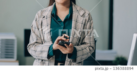 Determined asian businesswoman works late in a modern office, confidently analyzing data on her laptop, embodying success and professionalism with a smile Determined asian businesswoman works late in a modern office, confidently analyzing data on her laptop, embodying success and professionalism with a smile 136388894