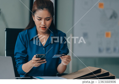 Young businesswoman is holding two credit cards with a worried expression, trying to decide which one to use to pay off her debt Young businesswoman is holding two credit cards with a worried expression, trying to decide which one to use to pay off her debt 136388906