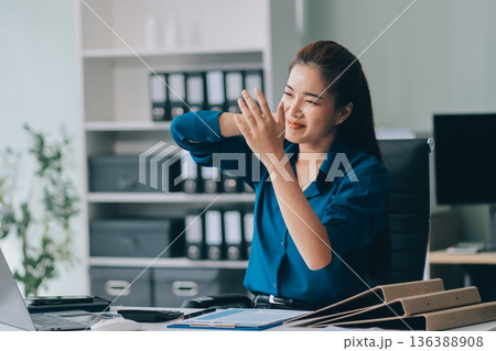 Asian businesswoman experiencing neck and shoulder pain, stretching during long hours working on computer at office Asian businesswoman experiencing neck and shoulder pain, stretching during long hours working on computer at office 136388908