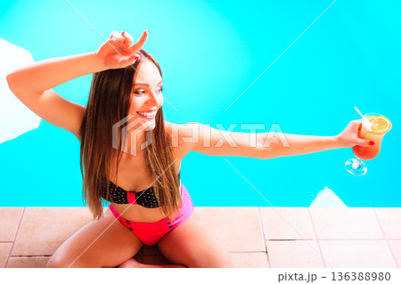 Woman with cocktail drink at swimming pool edge. 136388980