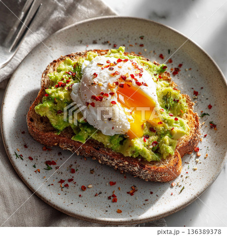 Sourdough toast topped with mashed avocado and a poached egg served on a white plate at a kitchen table Sourdough toast topped with mashed avocado and a poached egg served on a white plate at a kitchen table 136389378