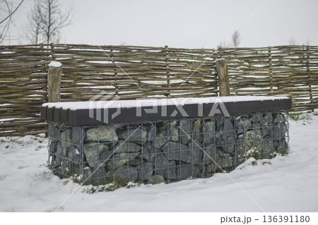 Snow-covered bench in a nature park. Snow-covered bench with rustic wooden fence. Concept of winter and winter nature. Snow-covered bench in a nature park. Snow-covered bench with rustic wooden fence. Concept of winter and winter nature. 136391180