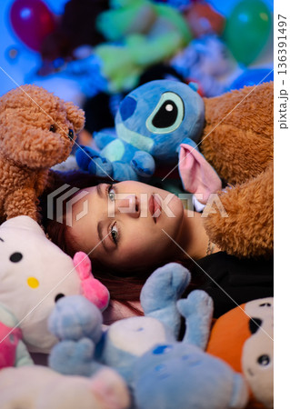 A young woman lies on the floor surrounded by many plush toys. A young woman lies on the floor surrounded by many plush toys. 136391497