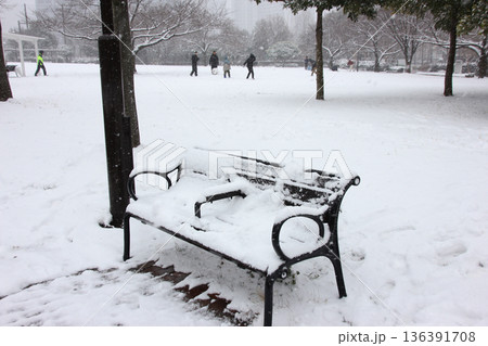 雪に埋もれたベンチの向こうで楽しそうに遊ぶ人たち 136391708