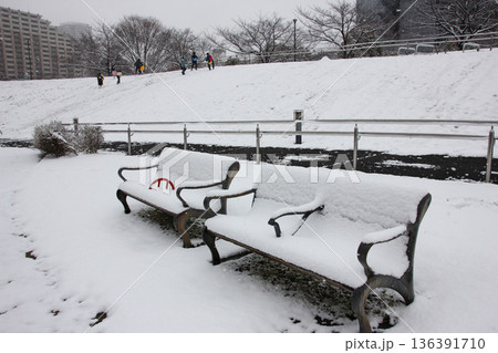 雪に埋もれたベンチの向こうは元気に戯れる子供達 136391710