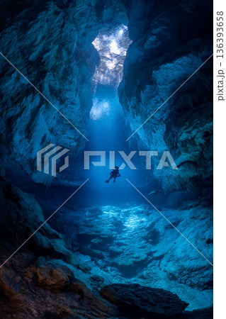 A serene wide shot of a secluded cenote with a freediver exploring its illuminated underwater caves, emphasizing a magical, hidden world. 136393658