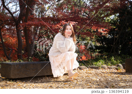秋の公園で紅葉を背景にしている笑顔の若い女性 136394119