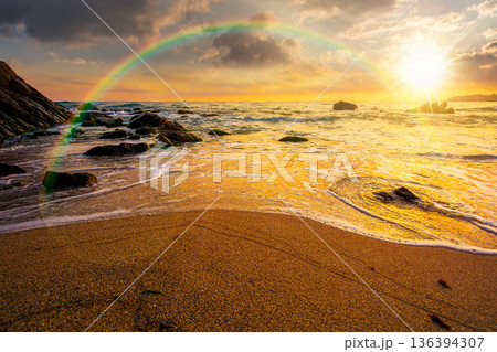 beautiful sunset over empty sandy beach at the sea. white foam rolling on to the shore near boulder in evening light with rainbow. perfect summer vacation concept. awesome weekend. low angle view beautiful sunset over empty sandy beach at the sea. white foam rolling on to the shore near boulder in evening light with rainbow. perfect summer vacation concept. awesome weekend. low angle view 136394307