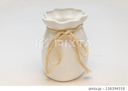 White ceramic vase tied with decorative rope on a light background. 136394558