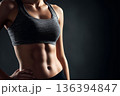 Fit faceless woman in sportswear demonstrating toned abs with copy space. Female athlete after an intense workout. Fitness motivation, active lifestyle, exercise, personal transformation journey. 136394847