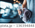 Close up of faceless man holding towel and water bottle in gym with copy space. Post workout wellness recovery, hydration, healthy lifestyle, motivation, daily fitness, wellness discipline. 136394848
