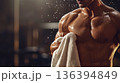 Strong muscular faceless man standing in dim gym environment with sweat droplets, wiping down after an intense workout. Fitness, copy space, strength training program, bodybuilding, athletic. 136394849
