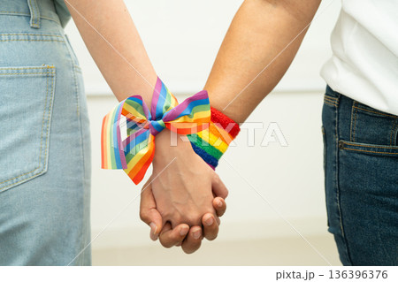 Asian LGBT couple woman holding hand wearing rainbow wristband. 136396376
