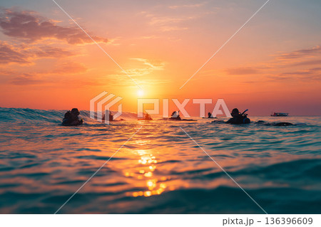 The serene scene of multiple snorkelers gently drifting across calm, shallow water at sunset, their forms silhouetted softly. The serene scene of multiple snorkelers gently drifting across calm, shallow water at sunset, their forms silhouetted softly. 136396609