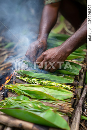 A close-up of "Lovo" (earth oven) cooking in progress, with smoky steam rising from banana leaves, highlighting traditional methods. 136396803