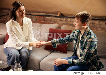 Teenage boy holding hands with female psychologist during therapy session. 136396819