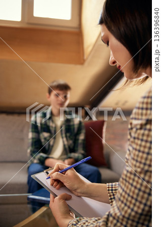 Psychologist writing notes during teenage therapy session. 136396840
