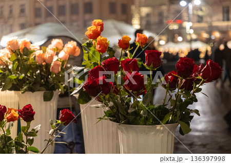 Vibrant bouquets of red, orange, and light peach roses are beautifully displayed in white vases, creating a romantic ambiance at an evening city market Vibrant bouquets of red, orange, and light peach roses are beautifully displayed in white vases, creating a romantic ambiance at an evening city market 136397998