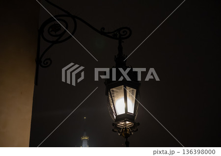An antique street lamp casts a warm glow from its ornate wrought-iron bracket, illuminating a dark historic alley and creating a mysterious vintage ambiance 136398000
