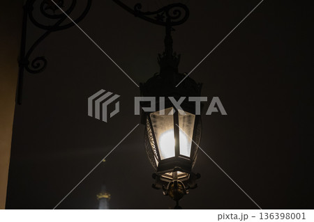 Ornate vintage street lamp glowing brightly against a dark night, showcasing intricate metalwork and classic design for an elegant old-world charm 136398001