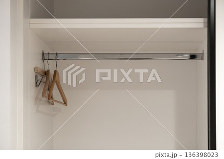 Clean empty white wardrobe interior with modern wooden hangers on a shining chrome rod and top shelf, representing home organization and storage solutions Clean empty white wardrobe interior with modern wooden hangers on a shining chrome rod and top shelf, representing home organization and storage solutions 136398023