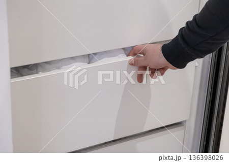 Man's hand reaching to open a white minimalist drawer filled with clean white linens, highlighting efficient home organization and storage solutions for a tidy space Man's hand reaching to open a white minimalist drawer filled with clean white linens, highlighting efficient home organization and storage solutions for a tidy space 136398026