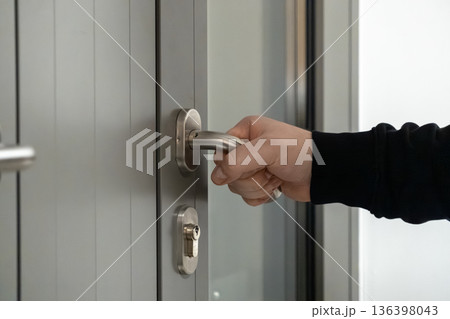 Hand gripping a modern silver door handle with a keyhole, signifying access, security, and an important entry or exit for home or business premises 136398043