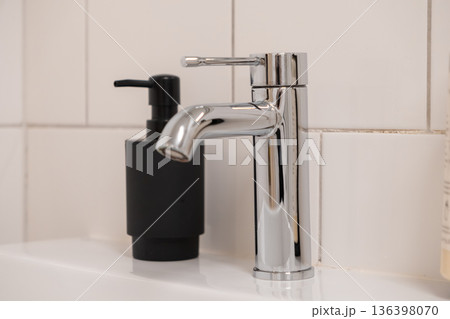 Bright chrome faucet and elegant black soap dispenser grace a pristine white sink, symbolizing modern bathroom design and essential daily hygiene Bright chrome faucet and elegant black soap dispenser grace a pristine white sink, symbolizing modern bathroom design and essential daily hygiene 136398070