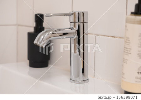 Modern chrome bathroom faucet with sleek design and shiny finish on a pristine white ceramic sink, essential for personal hygiene and home sanitation Modern chrome bathroom faucet with sleek design and shiny finish on a pristine white ceramic sink, essential for personal hygiene and home sanitation 136398071