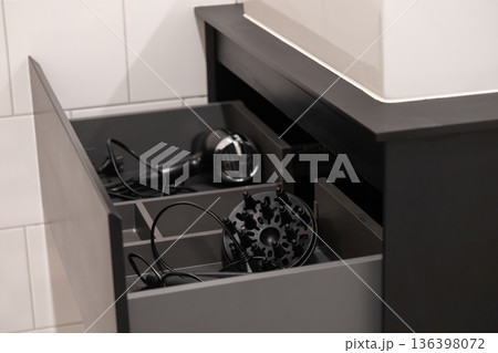 Open dark gray bathroom drawer revealing a modern hair dryer and diffuser, illustrating efficient personal care product organization in a contemporary home 136398072