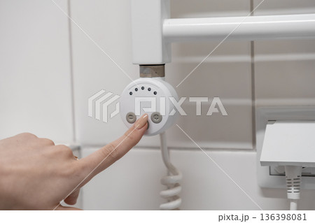 Woman's finger precisely adjusts the modern digital thermostat for a white heated towel rail, optimizing bathroom temperature and personal comfort Woman's finger precisely adjusts the modern digital thermostat for a white heated towel rail, optimizing bathroom temperature and personal comfort 136398081