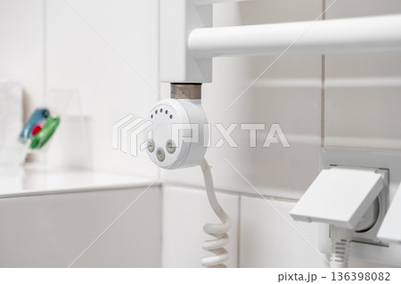 White electric towel warmer with a digital control unit and coiled power cord, providing comfortable heating and energy efficiency for a modern bathroom 136398082
