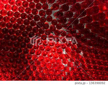 Vibrant red glass bottles artfully arranged and illuminated from behind, forming a captivating abstract pattern and modern design installation, evoking luxury and celebration 136398092