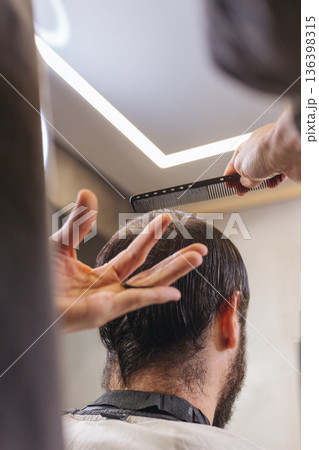 Barber cutting male client hair with scissors and comb. Close up of professional haircut process, precision technique, men grooming service in modern barbershop. Barber cutting male client hair with scissors and comb. Close up of professional haircut process, precision technique, men grooming service in modern barbershop. 136398315