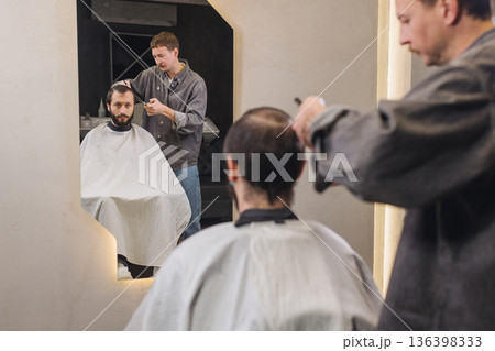 Barber cutting male client hair with scissors and comb. Close up of professional haircut process, precision technique, men grooming service in modern barbershop. 136398333