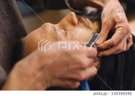 Close up of professional barber shaving male neck with straight razor in barbershop. Beard contouring, classic wet shave, men grooming service and barber work process concept. 136398346