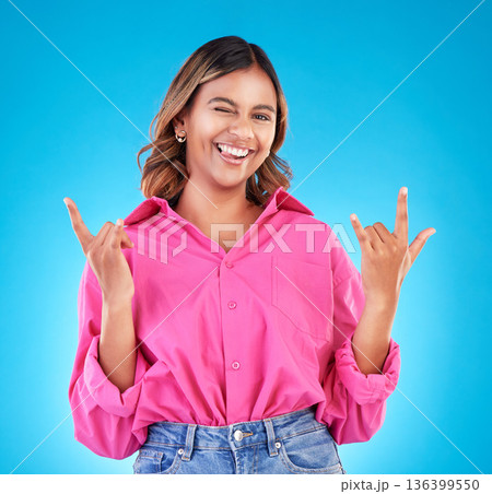 Wink, portrait and woman with rocker hands in studio for freedom, happy and positive attitude on blue background. Smile, face and female with rockstar emoji, sign or punk gesture, good mood or vibes Wink, portrait and woman with rocker hands in studio for freedom, happy and positive attitude on blue background. Smile, face and female with rockstar emoji, sign or punk gesture, good mood or vibes 136399550