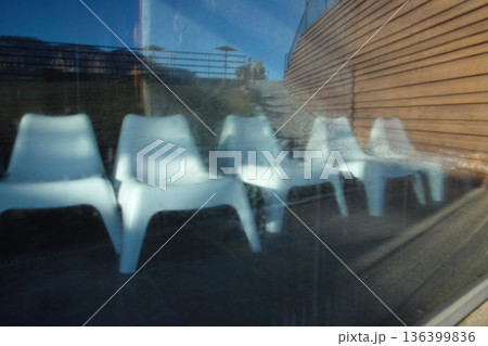 Reflection of white chairs on glass wall at sunset 136399836