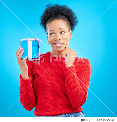 Thinking, winner and black woman with a present, box and celebration against a blue studio background. Female person, doubt or model with a gift, giveaway product or package with surprise and curious 136399918