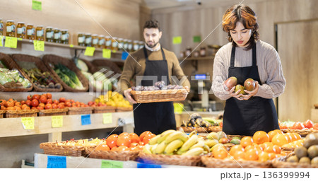 Portrait of man and woman - employees of grocery supermarket with various vegetables and fruits in their hands Portrait of man and woman - employees of grocery supermarket with various vegetables and fruits in their hands 136399994