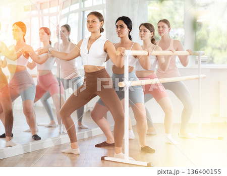 Girl performing demi plie during group barre fitness session Girl performing demi plie during group barre fitness session 136400155
