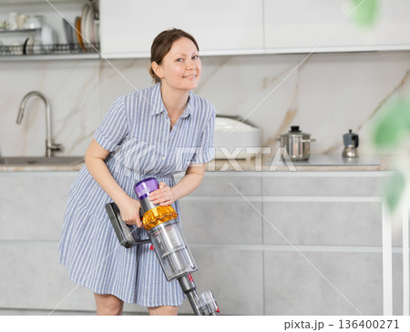 Housewife using vacuum cleaner removes dust in room 136400271